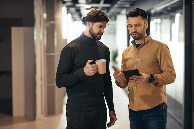 Colleghi di sesso maschile che discutono di un progetto di avvio aziendale utilizzando la tavoletta digitale mentre si cammina nella sala dell'ufficio