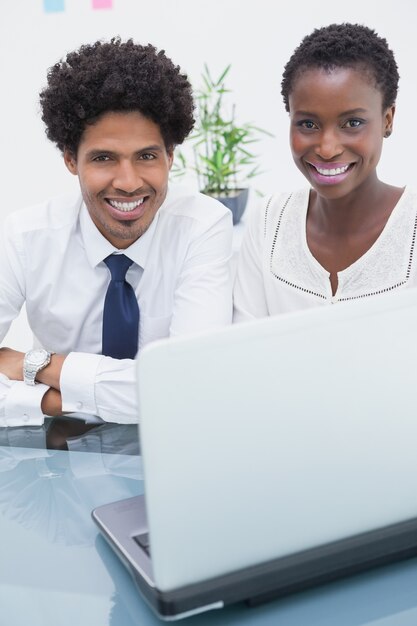 Colleghi felici che utilizzano computer portatile e che guarda l&#39;obbiettivo