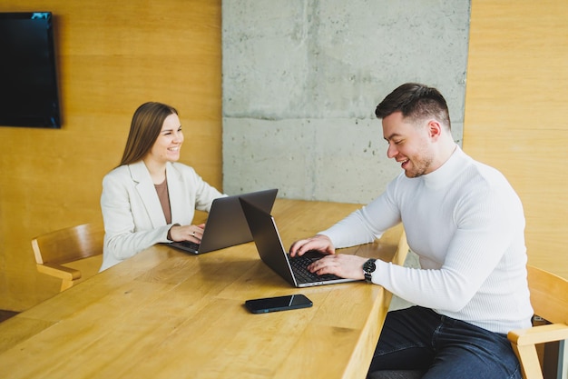 Colleghi maschi e femmine lavorano a un tavolo di legno su laptop e parlano Concetto di cooperazione aziendale e lavoro di squadra Giovani colleghi in ufficio Persone moderne di successo