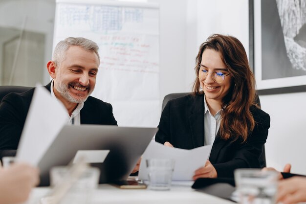 Colleghi sorridenti che fanno scartoffie Partner commerciali che leggono i contratti Imprenditori felici che firmano documenti alla conferenza