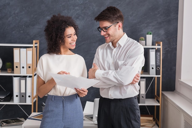 Colleghi sorridenti che parlano e discutono di documenti mentre sono in piedi in ufficio