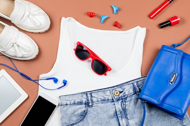 Collezione di abbigliamento estivo femminile, stile casual rilassato. Top bianco, blue jeans, mocassini, accessori rossi e blu, gadget.
