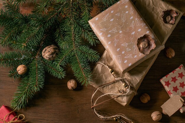 Collezione di scatole regalo di Natale in carta artigianale ecologica decorata da noci naturali e bastoncini di cannella su sfondo di legno con rami di abete. Concetto di regalo di Natale ecologico. Lay piatto