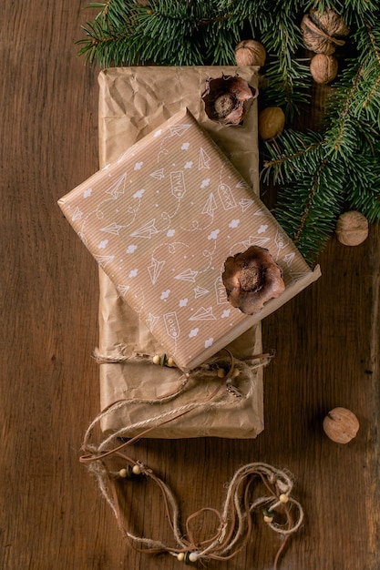 Collezione di scatole regalo di Natale in carta artigianale riciclata ecologica decorata da noci naturali e bastoncini di cannella su sfondo di legno con rami di abete. Concetto di regalo di Natale ecologico. Lay piatto