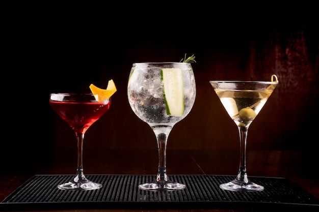 Collezione di tre bicchieri da cocktail tra cui gin tonic martini e vesper con oliva in supporto di gomma visti frontalmente