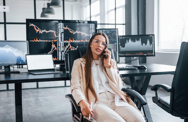 Colloqui per telefono Giovane agente di borsa femminile lavora al chiuso in ufficio Molti dei display