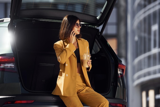 Colloqui per telefono Giovane donna alla moda in cappotto color bordeaux di giorno con la sua auto