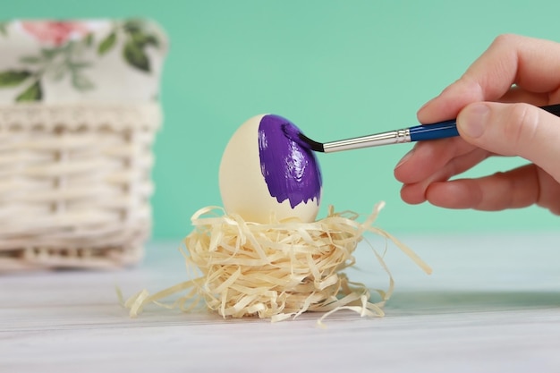 Colorare l'uovo di Pasqua in colore viola. Uovo in un nido su uno sfondo turchese sfocato