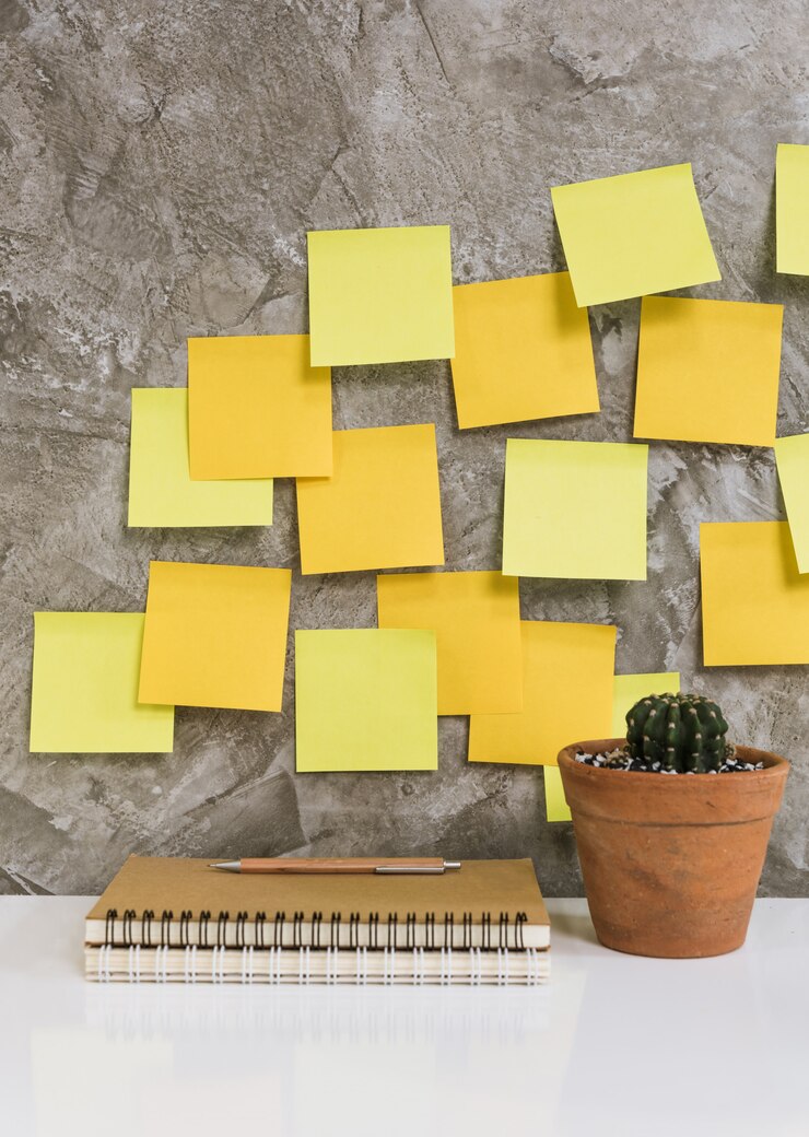 Colorato post-it, taccuino memo, matita, cactus in vaso di fiori sulla scrivania bianca sullo sfondo di cemento, concetto di spazio di lavoro
