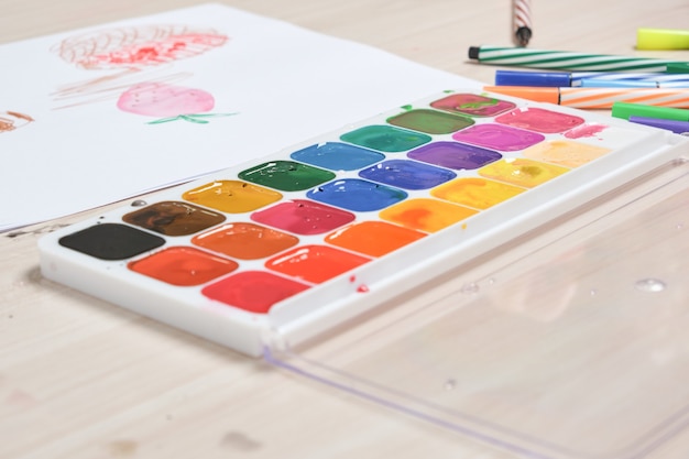 Colori ad acquerello e disegno di un bambino piccolo su un tavolo luminoso in legno, creatività dei bambini