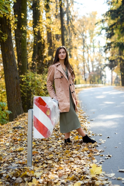 Colori autunnali. Bella donna in cappotto in posa nella foresta sul ciglio della strada