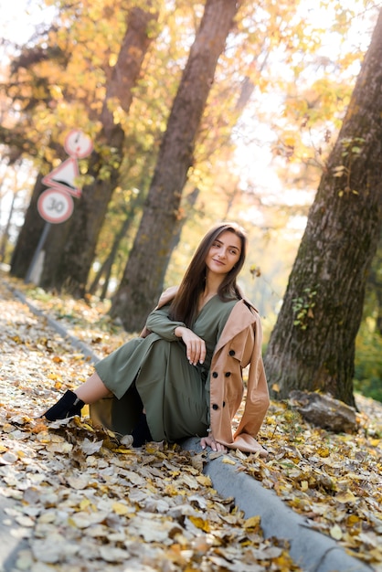 Colori autunnali. Bella donna in cappotto in posa nella foresta sul ciglio della strada