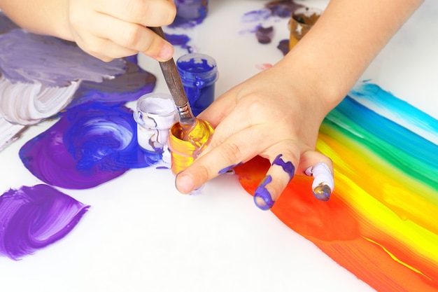 Colori della pittura di tiraggio della mano del bambino su un fondo bianco. creatività e hobby artistico