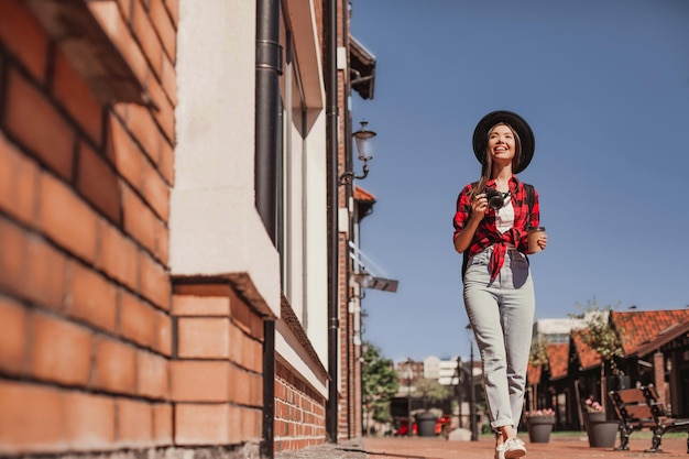 Colpo a figura intera di turista femminile con fotocamera che cammina in città