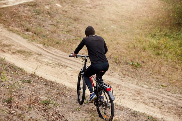 Colpo all'aperto del ciclista maschio che guida in salita lungo la strada campestre, trascorrendo la giornata libera in modo attivo