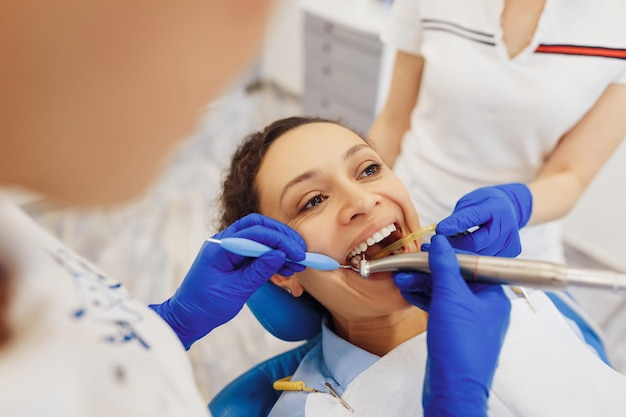 Colpo dall'alto di dottoressa e infermiera in guanti che effettuano cure mediche di denti femminili con strumenti dentali in clinica