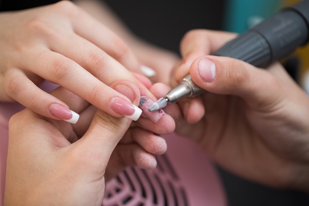 Colpo del primo piano del maestro utilizza una macchina elettrica per rimuovere lo smalto durante la manicure nel salone. Manicure hardware. Concetto di cura del corpo