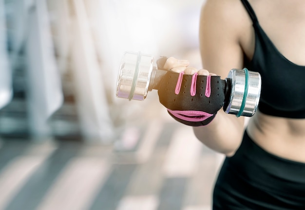 Colpo del primo piano della donna di forma fisica che alza i dumbbells alla palestra.