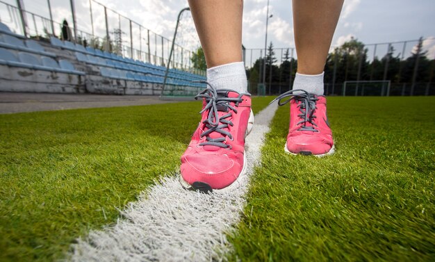 Colpo del primo piano della donna in scarpe da tennis rosa che corrono sul campo di erba