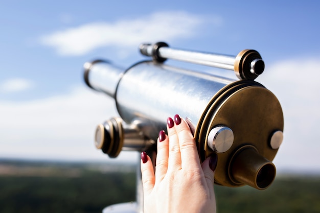 Colpo del primo piano della mano femminile che tiene il binocolo turistico contro il panorama della foresta