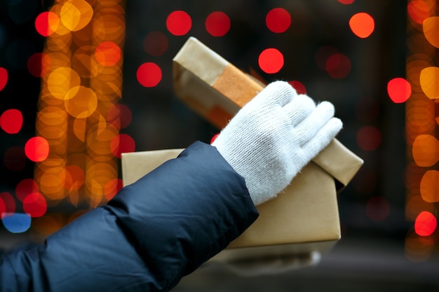 Colpo del primo piano delle mani femminili che tengono la confezione regalo sullo sfondo del bokeh. Spazio per il testo