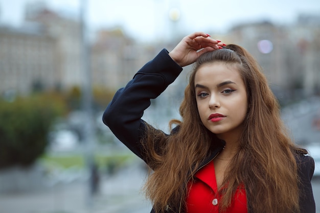 Colpo del primo piano di adorabile donna bruna con i capelli lunghi in posa nella città di sera. Spazio per il testo