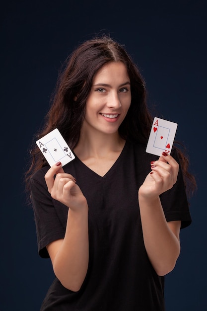 Colpo del primo piano di capelli ricci bruna in posa con carte da gioco nelle sue mani. Concetto di poker su sfondo nero. Casinò.