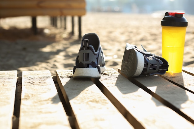 Colpo del primo piano di scarpe sportive femminili e bottiglia d'acqua in piedi sulla spiaggia. Spazio per il testo