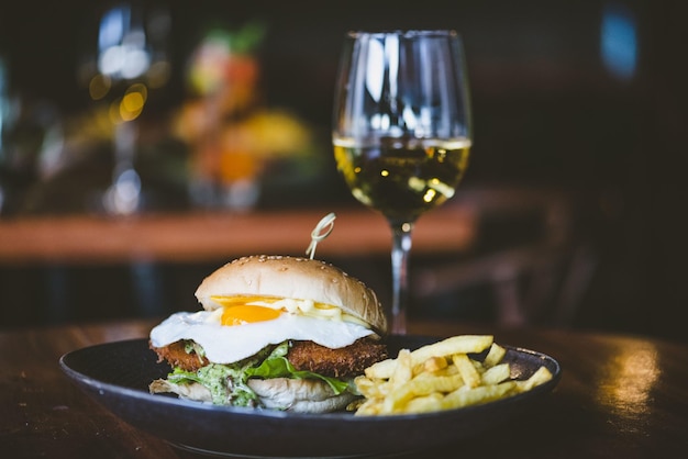 Colpo del primo piano di un delizioso hamburger con patatine fritte sul lato e un bicchiere di vino