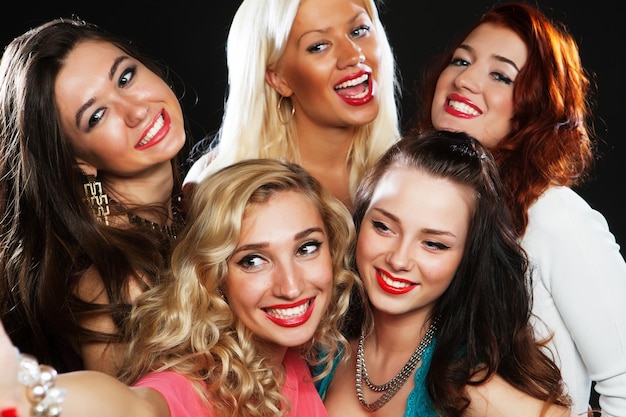 Colpo del primo piano di un gruppo di ragazze che ridono che fanno festa e prendono selfie con lo smartphone
