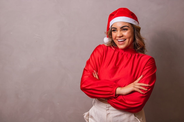 Colpo del primo piano di una bellissima giovane donna con cappello da Babbo Natale e braccia incrociate. buon Natale