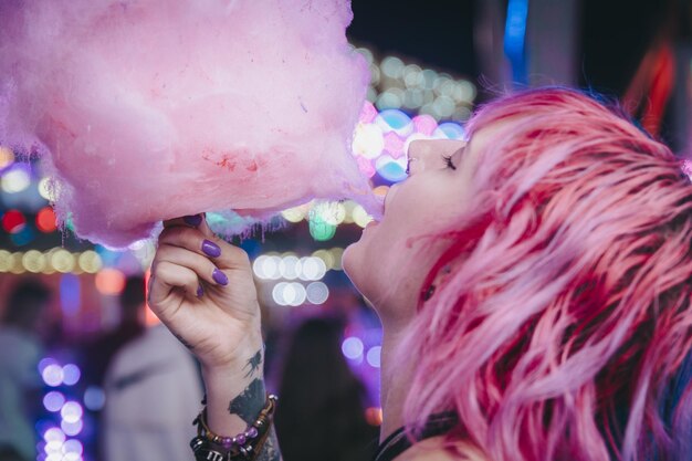 Colpo del primo piano di una giovane donna attraente che si diverte a mangiare zucchero filato in un parco di divertimenti