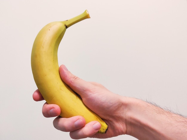 Colpo del primo piano di una mano che tiene una banana su uno sfondo bianco