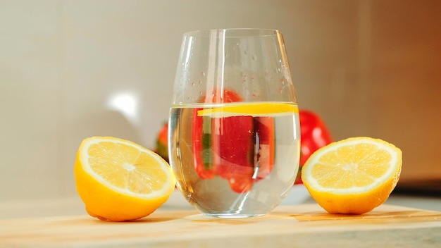 Colpo del primo piano di vetro con acqua tra due parti di limone tagliato su tavola da cucina in legno.