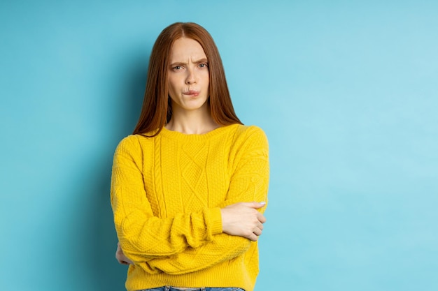 Colpo dell'interno di giovane femmina caucasica premurosa insoddisfatta con i capelli rossi, arricciando le labbra, guardando la telecamera con espressione dubbiosa e indecisa. Concetto di emozioni. Copia spazio.