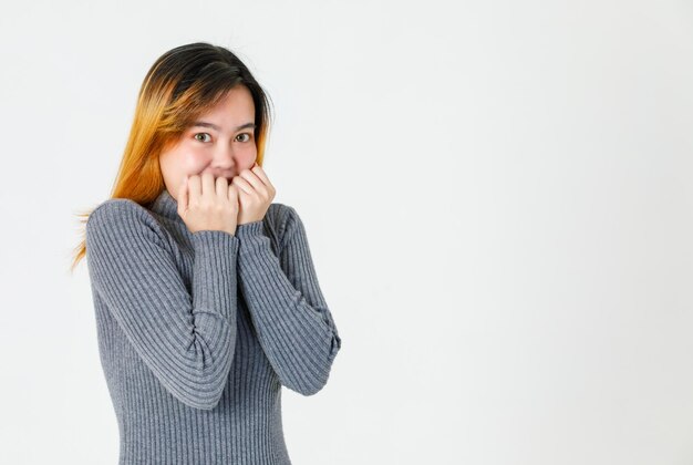 Colpo dello studio del primo piano del ritratto del modello femminile di capelli tinti giovani asiatici in maglione a collo alto grigio stare sorridente che tiene i pugni sul viso copertina sentirsi eccitante scioccante sorprendente incredibile su priorità bassa bianca.