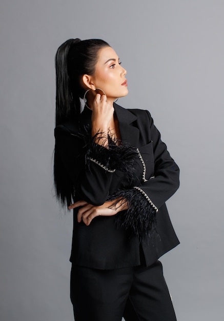 Colpo dello studio del ritaglio isolato ritratto del modello di modo elegante femminile asiatico millenario in vestito di pelliccia alla moda casual nero in piedi in posa sguardo alla macchina fotografica su sfondo grigio