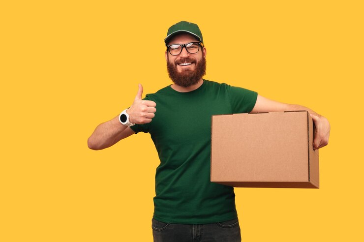 Colpo dello studio di un uomo di consegna sorridente che tiene una grande scatola e un pollice in su