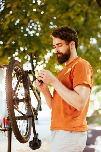 Colpo dettagliato di un giovane uomo caucasico sano all'aperto che esamina e mantiene la ruota della bicicletta con attrezzature professionali. Maschio attivo amante dello sport che trasporta un multitool specializzato per la riparazione di biciclette.