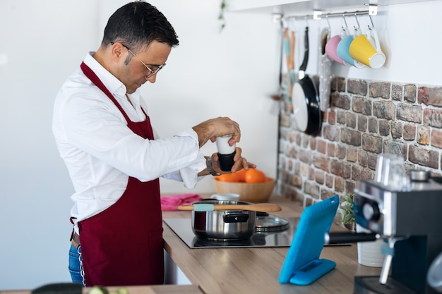 Colpo di bell'uomo che cucina mentre segue una ricetta sul tablet digitale in cucina a casa.