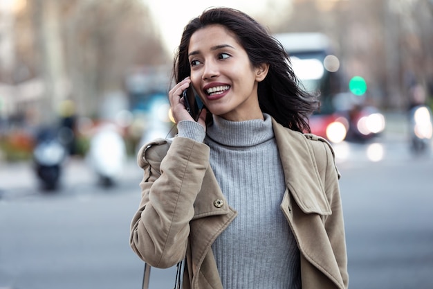 Colpo di bella giovane donna che parla al telefono cellulare mentre si cammina per strada.