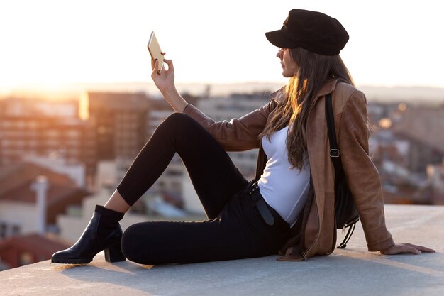 Colpo di bella giovane donna che si fa un selfie con il cellulare mentre è seduta sul tetto.