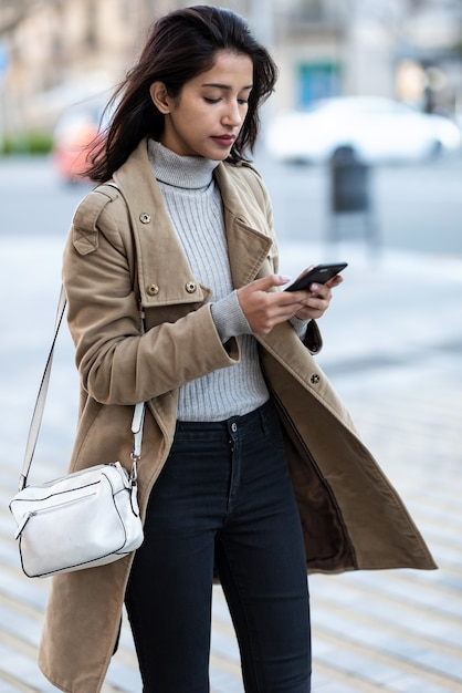 Colpo di bella giovane donna che usa il suo smartphone mentre cammina per strada.