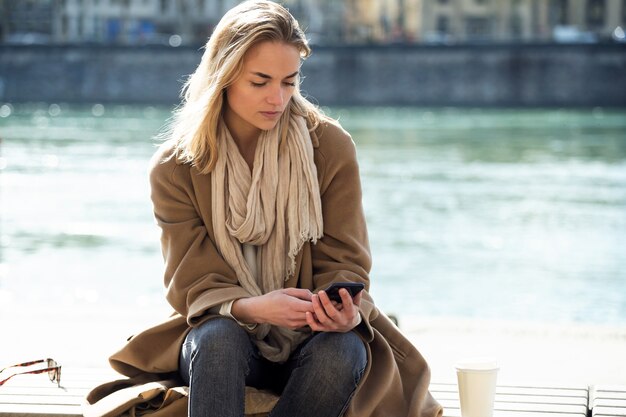 Colpo di bella giovane donna che usa il suo telefono cellulare vicino al fiume in città.