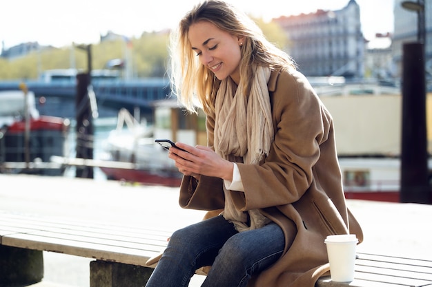 Colpo di bella giovane donna che usa il suo telefono cellulare vicino al fiume in città.