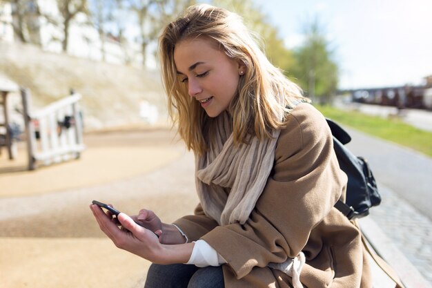 Colpo di bella giovane donna che usa il suo telefono cellulare vicino al fiume in città.