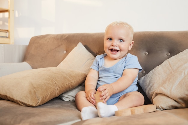 colpo di carino piccolo neonato che indossa abiti azzurri, seduto sul divano sorridendo