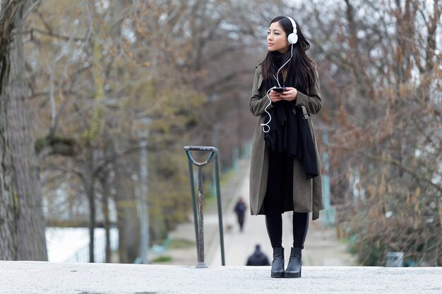 Colpo di giovane donna abbastanza asiatica che ascolta musica con il suo smartphone in strada.