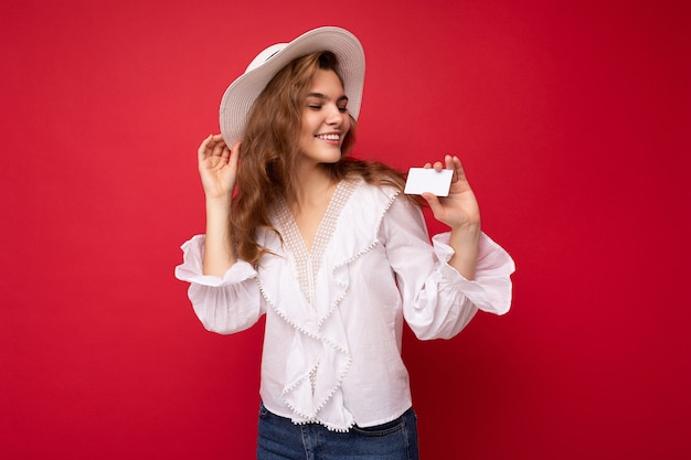 Colpo di giovane donna bionda scura sorridente positiva attraente che indossa camicetta bianca e cappello bianco