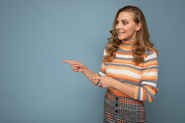 Colpo di giovane donna positiva dai capelli ondulati bionda felice che indossa un pullover a righe isolato su blue